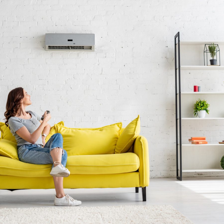 pretty young woman sitting on yellow sofa under air conditioner at home